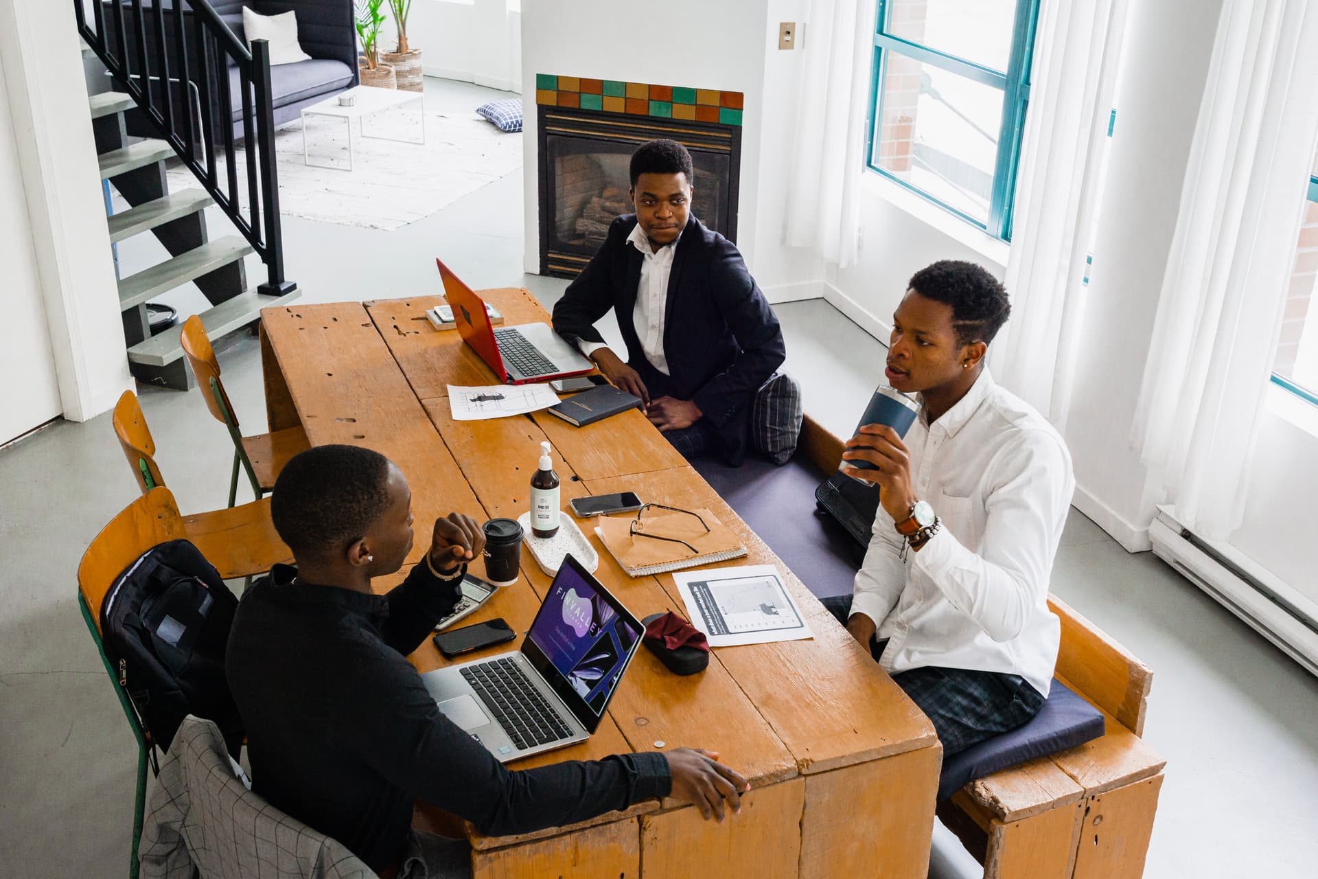 A small team gathered around a wooden table, laptops open, mid-conversation